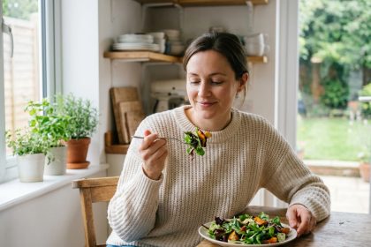 Femme souriante mangeant une salade dans une cuisine lumineuse