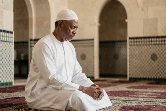 Homme en djellaba blanche effectuant une prière islamique dans une mosquée française au décor traditionnel en zellige