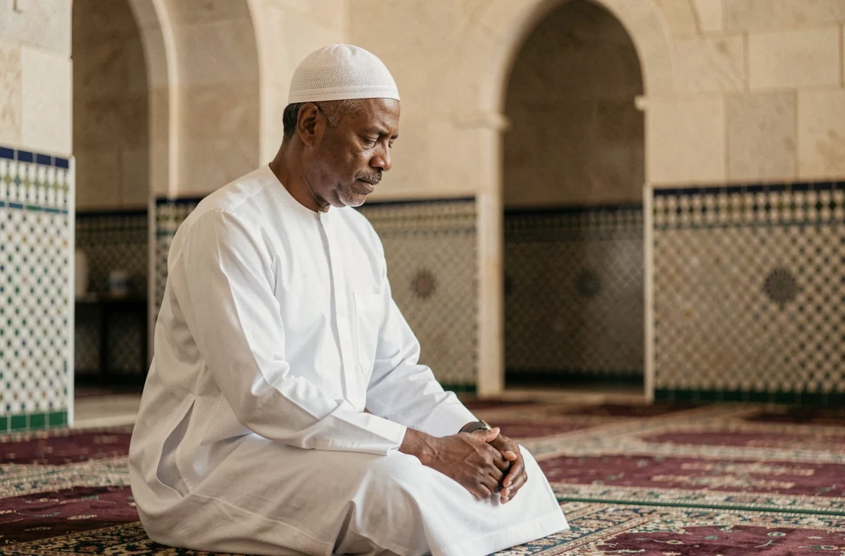 Homme en djellaba blanche effectuant une prière islamique dans une mosquée française au décor traditionnel en zellige
